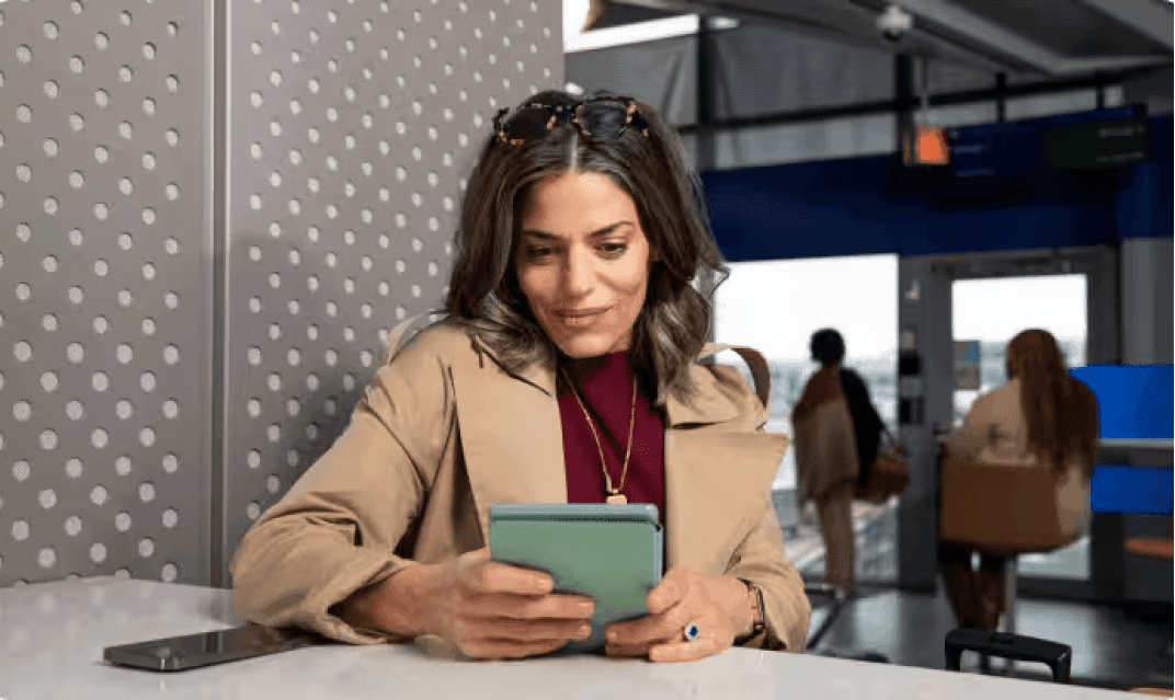 A woman viewing a small tablet while sitting at a counter.
