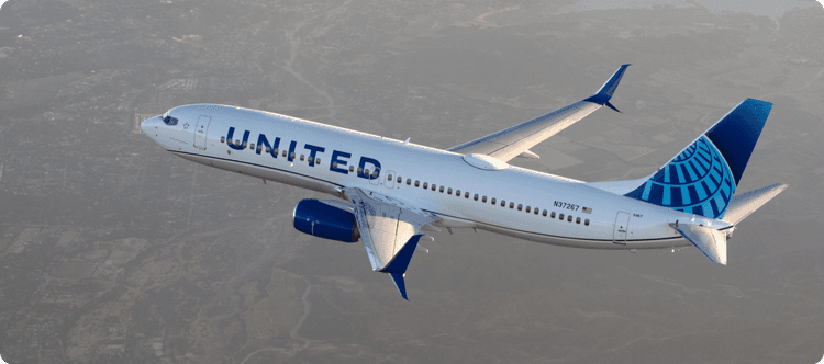 United Airlines airplane flying over mountainous landscape with cloudy sky