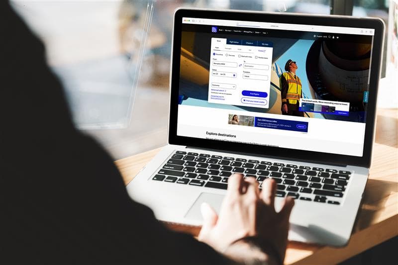 A person at a lounge typing on their laptop keyboard searching for a flight on United’s website