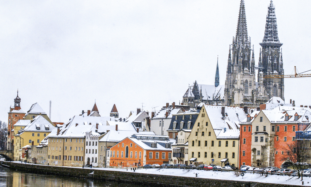 A long shot of a European city with a church and snow covered houses that sit along a man made canal.