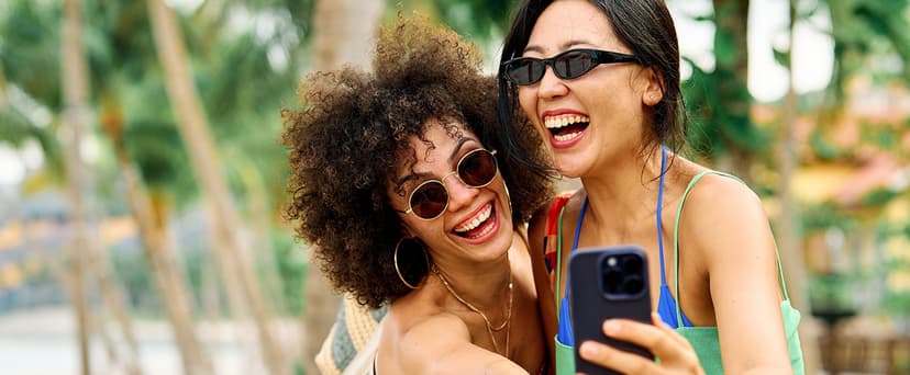 2 women friends wearing sunglasses smiling and taking a selfie outdoors in summer