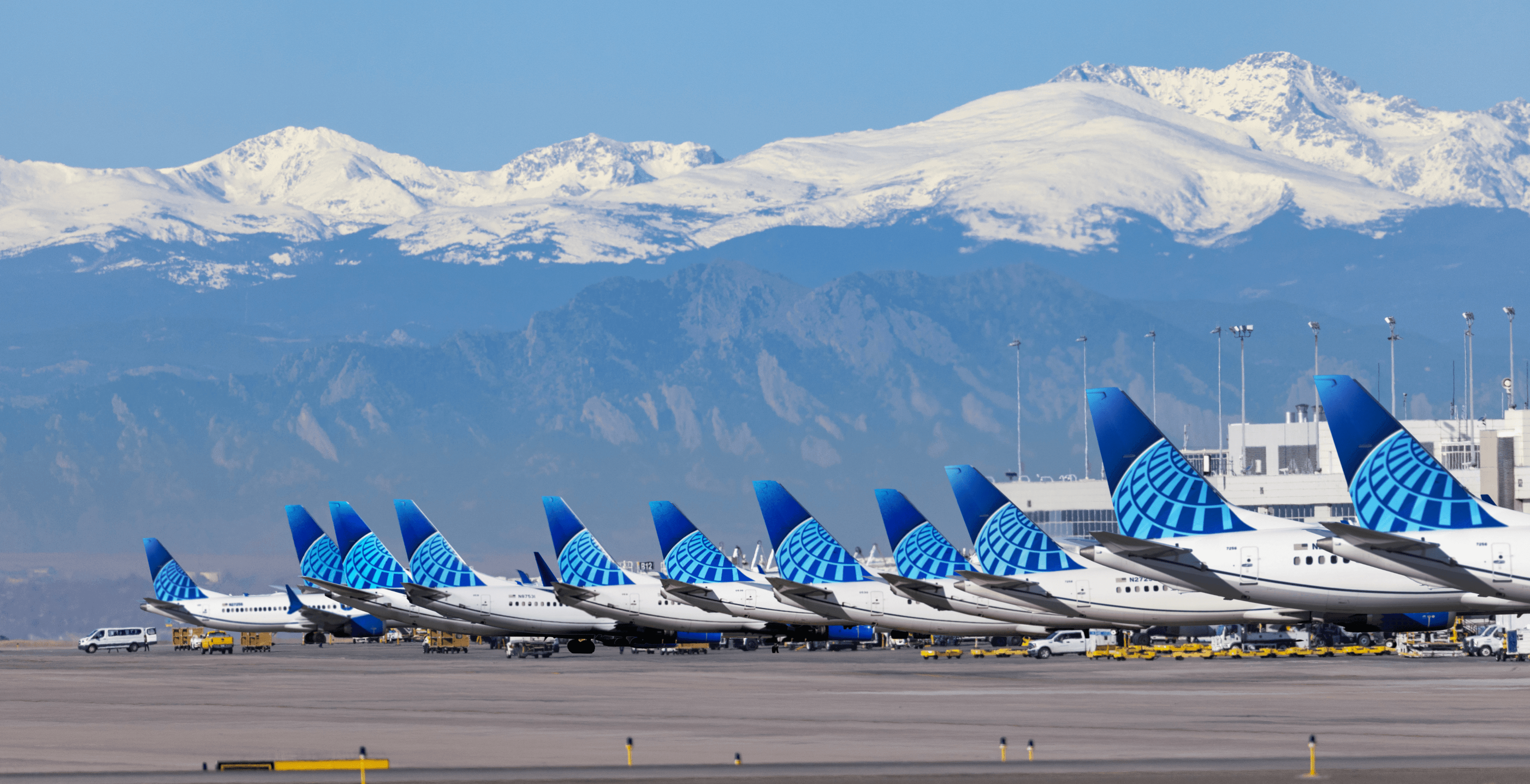 A row of United Airline planes parked at their airport terminals with snow capped mountains in the background