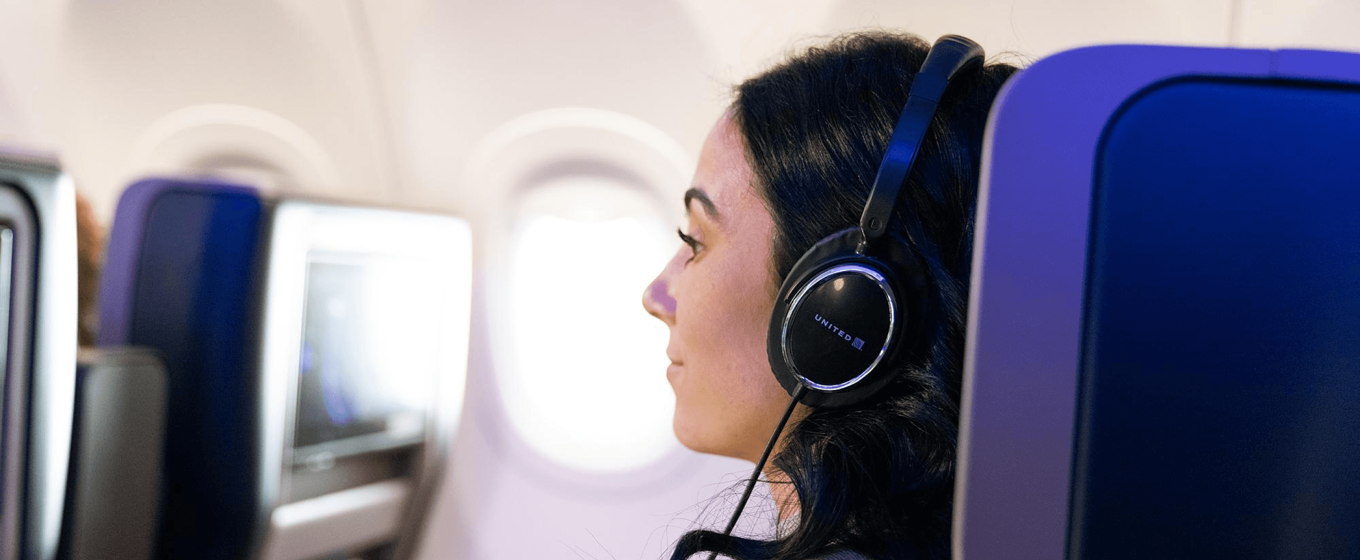 A traveler with headphones on watching an inflight entertainment screen on a plane.