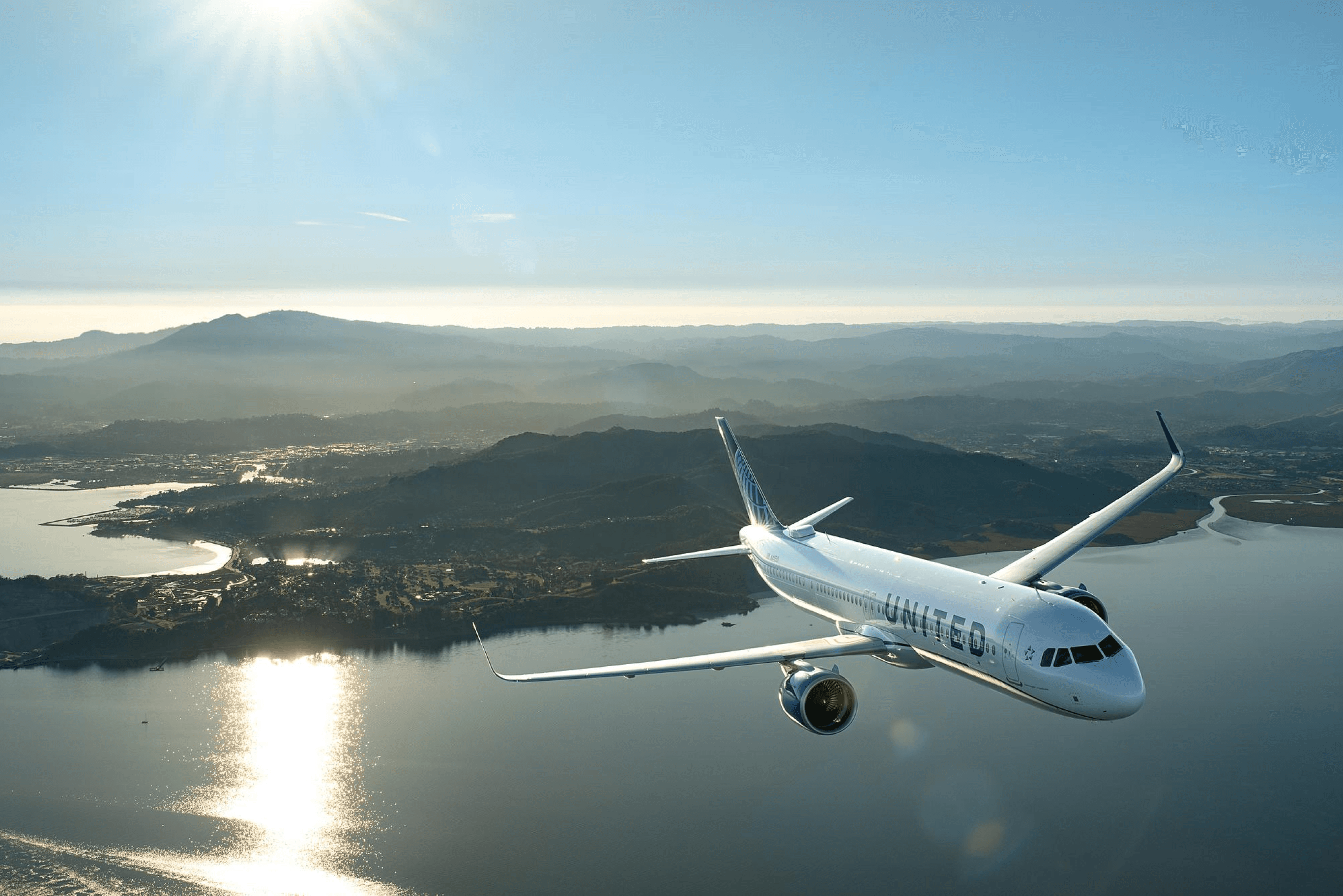 A United plane flying above a lake and mountains.