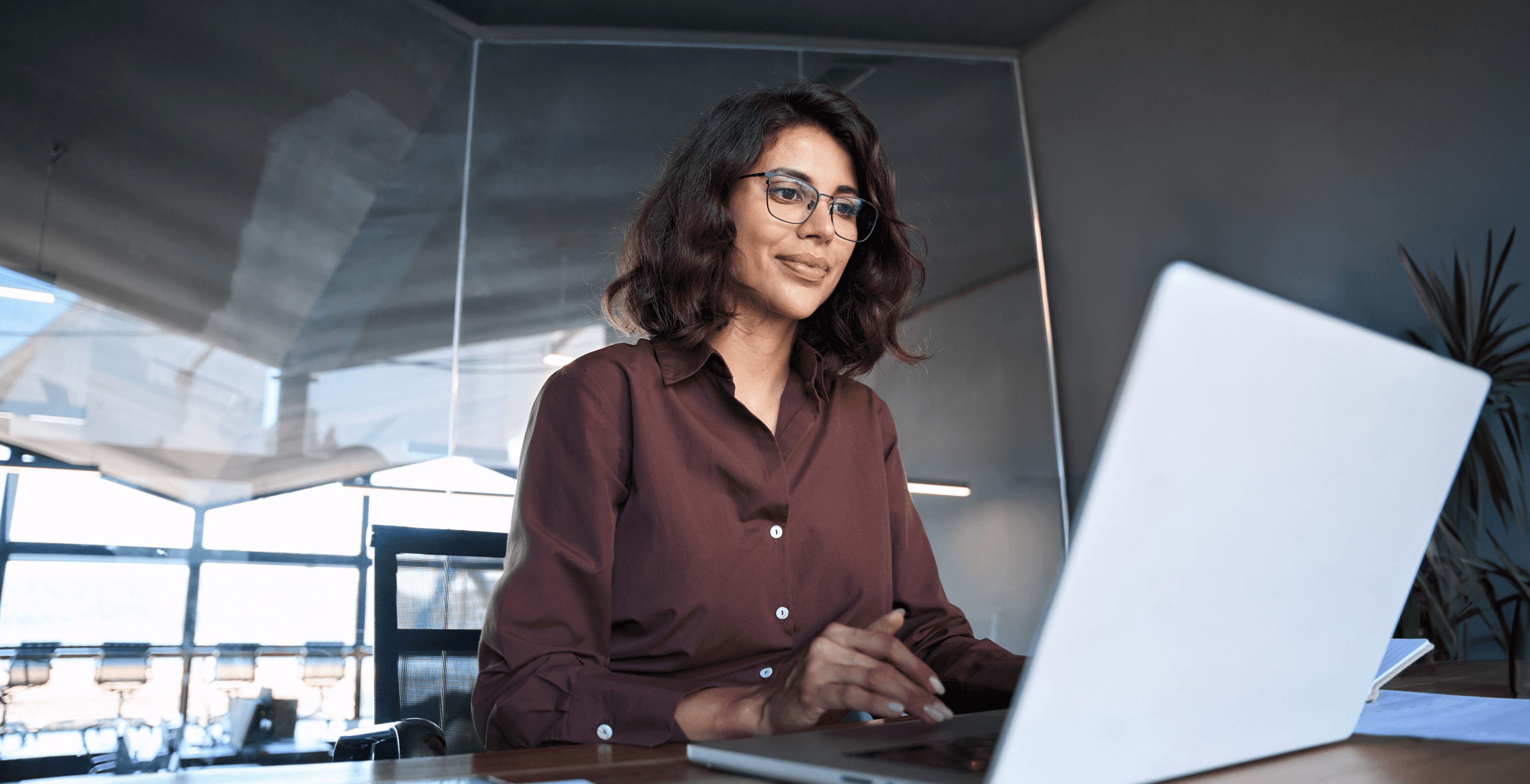 A blue hued moody, tightly cropped, photo of a woman typing on a laptop keyboard with her cell phone facing up by its side